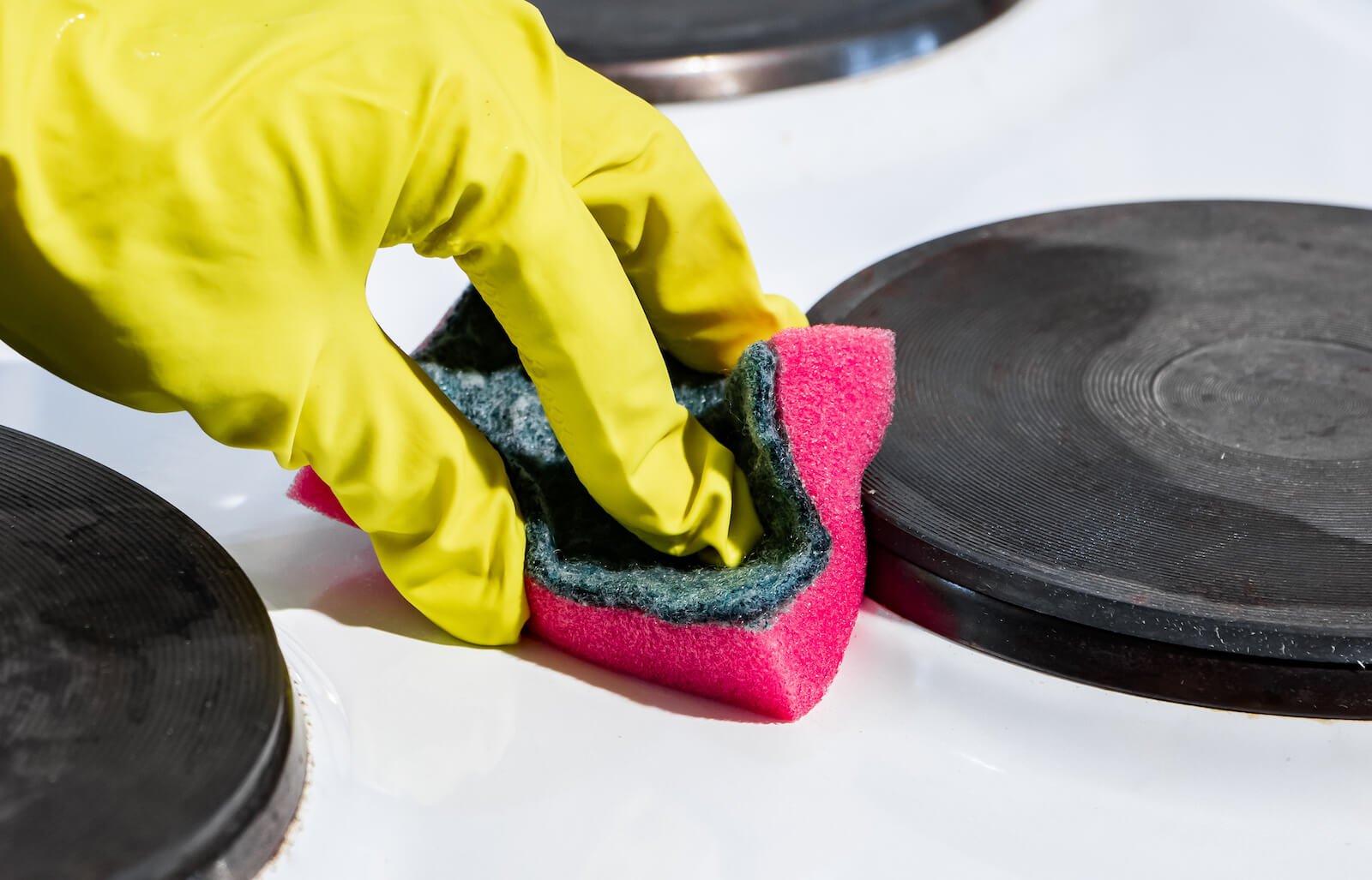 Hand scrubbing stovetop with a sponge