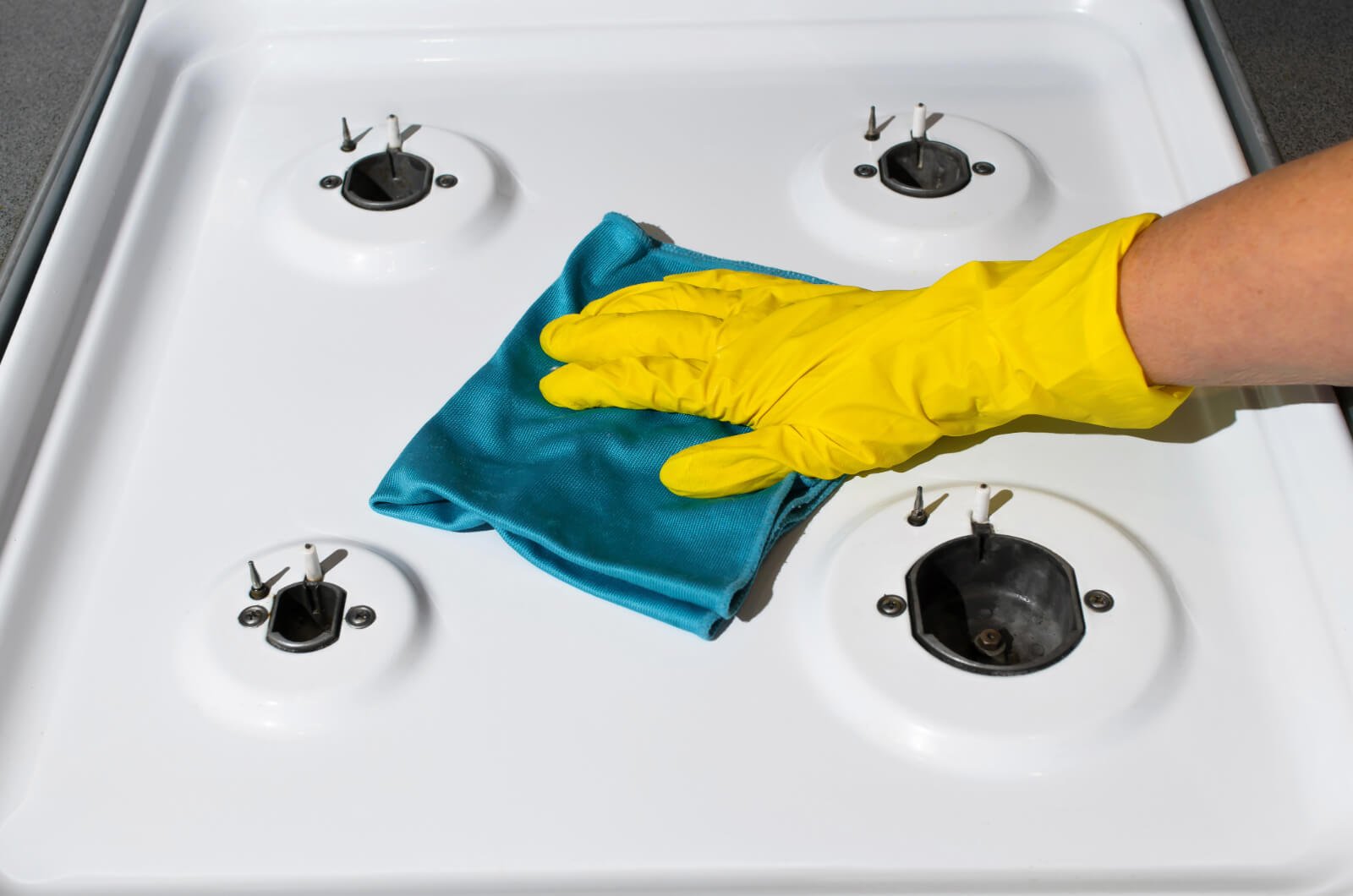 Gloved hand cleaning stovetop with rag