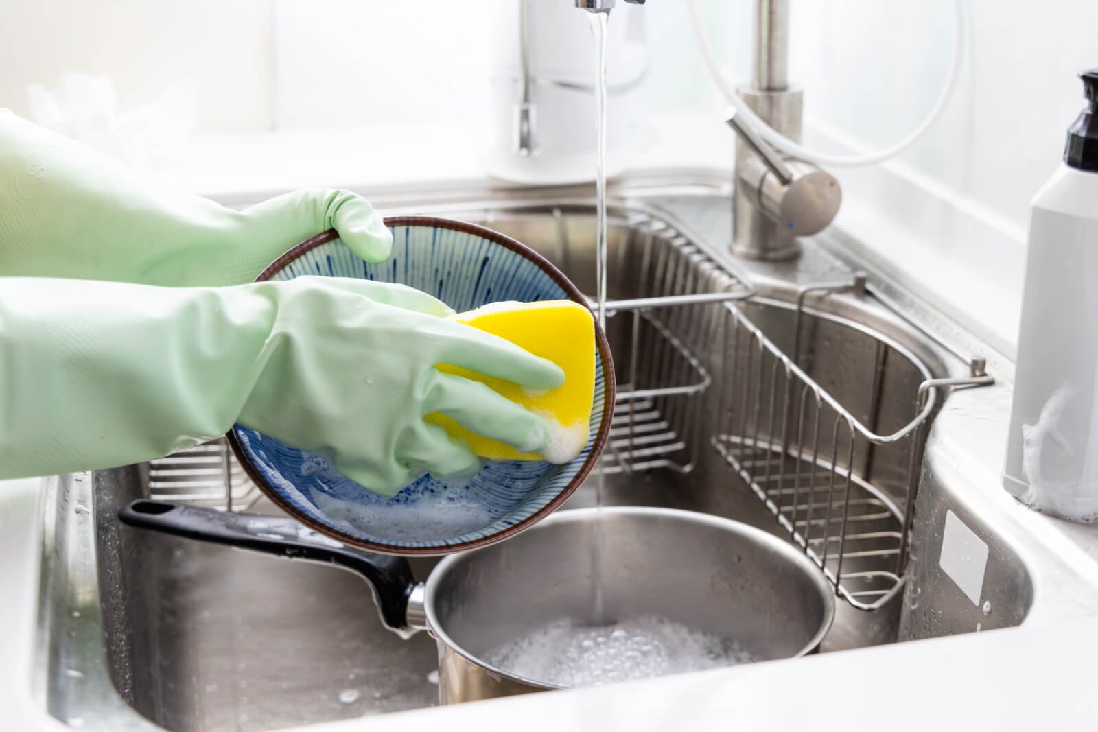 Hands wearing latex gloves washing dishes in sink